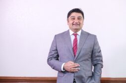 Rashid Khalani, CEO of Aga Khan University Hospital, in a grey suit with a red patterned tie, smiling confidently against a plain background. Portrait of Rashid Khalani, Chief Executive Officer of Aga Khan University Hospital, standing in a grey business suit, symbolising leadership in healthcare transformation.