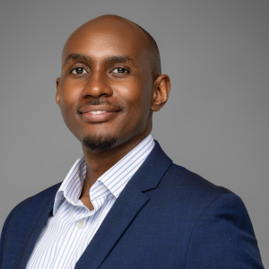 Kenneth Muhangi, a distinguished Ugandan lawyer, lecturer, and reform advocate, is pictured standing confidently in a professional setting, dressed in a navy-blue suit and a light-striped shirt. He is a Partner at KTA Advocates, a leading law firm specializing in technology, intellectual property, sustainability, and policy law. Known for his calm, thoughtful demeanor and sharp intellect, Kenneth embodies a new generation of legal leadership rooted in integrity, practical service, and ethical reform. His career reflects a commitment to mentorship, innovation, and institutional strengthening, while his personal philosophy balances impact, mindfulness, and faith-based purpose. Through his work in Uganda and across East Africa, he continues to champion technology-driven legal reform, education, and empowerment of young lawyers, promoting a legal profession defined by discipline, collaboration, and social responsibility.