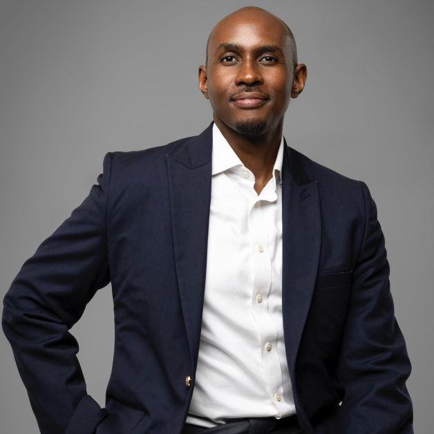 Kenneth Muhangi, a distinguished Ugandan lawyer, lecturer, and reform advocate, is pictured standing confidently in a professional setting, dressed in a navy-blue suit and a light-striped shirt. He is a Partner at KTA Advocates, a leading law firm specializing in technology, intellectual property, sustainability, and policy law. Known for his calm, thoughtful demeanor and sharp intellect, Kenneth embodies a new generation of legal leadership rooted in integrity, practical service, and ethical reform. His career reflects a commitment to mentorship, innovation, and institutional strengthening, while his personal philosophy balances impact, mindfulness, and faith-based purpose. Through his work in Uganda and across East Africa, he continues to champion technology-driven legal reform, education, and empowerment of young lawyers, promoting a legal profession defined by discipline, collaboration, and social responsibility.