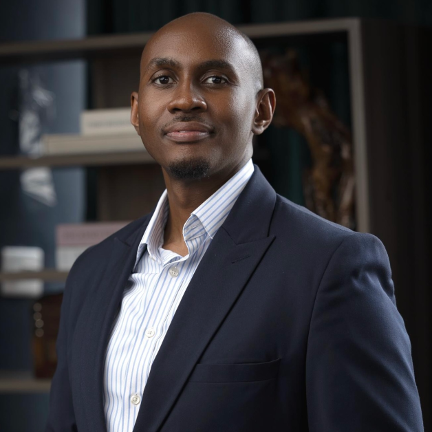 Kenneth Muhangi, a distinguished Ugandan lawyer, lecturer, and reform advocate, is pictured standing confidently in a professional setting, dressed in a navy-blue suit and a light-striped shirt. He is a Partner at KTA Advocates, a leading law firm specializing in technology, intellectual property, sustainability, and policy law. Known for his calm, thoughtful demeanor and sharp intellect, Kenneth embodies a new generation of legal leadership rooted in integrity, practical service, and ethical reform. His career reflects a commitment to mentorship, innovation, and institutional strengthening, while his personal philosophy balances impact, mindfulness, and faith-based purpose. Through his work in Uganda and across East Africa, he continues to champion technology-driven legal reform, education, and empowerment of young lawyers, promoting a legal profession defined by discipline, collaboration, and social responsibility.