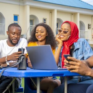 Four students sitting outdoors around a laptop and smartphones, discussing and reviewing study abroad options together.