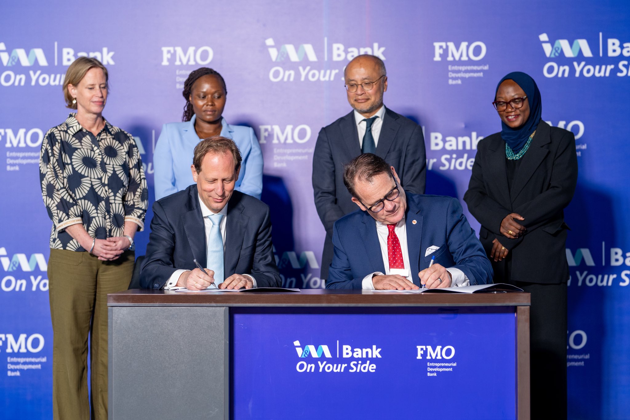 FMO Co-Chief Investment Officer Huib-Jan de Ruijter (left) and I&M Bank Uganda CEO Robin Bairstow sign the Memorandum of Understanding following the announcement of a USD 20 million financing partnership. Standing behind them (left–right) are Natalie den Breugom, Deputy Director for Sustainable Economic Development at the Dutch Ministry of Foreign Affairs; Faith Kathambi, Investment Officer – Financial Institutions at FMO; René Idzenga, Head of State-Owned Enterprises at the Dutch Ministry of Finance; and Nadia Mindra, Head of Treasury at I&M Bank Uganda.